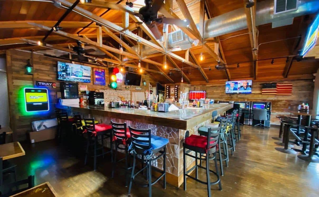 The bar and dining area inside Drews Brews and Grille, with TVs and string lighting under a wood ceiling
